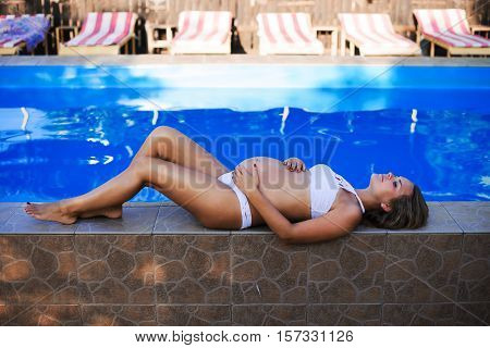 Beautiful Pregnant Woman Sun Tanning Relaxed At Blue Pool With Green Bikini