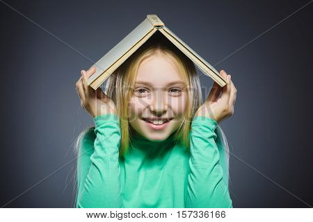 wondering girl with book over head. Closeup Portrait of handsome teen in casual shirt on grey background. studies concept.
