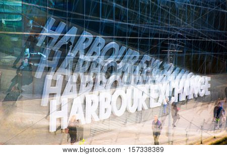 Multiple exposure effect image. Office workers walking against of Harbour Exchange sign
