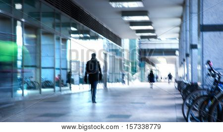 Abstract, blurred image of people walking via long tunnel with light at the background.
