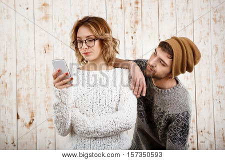 Young handsome man unnerve his girlfriend looking at phone over wooden background. Copy space.