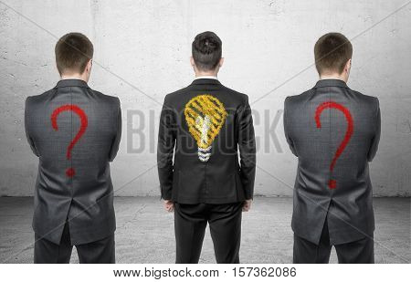 Three businessmen standing with drawing of light bulb and question marks on his back. Business and management. Solving problems. Having ideas.