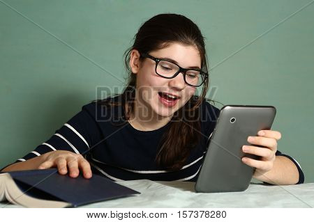 teenager lazy girl in myopia glasses play online game on tablet refuse to read book laughing entertain herself