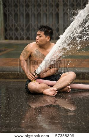 Bangkok, Thailand - April 13, 2008 : 
During Songkran the Thai New Year's festival. A man sitting on the street with a water pump.