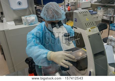 Saint-Petersburg Russia - November 16 2016: A member of the laboratory of department of Advanced Studies biotech companies Biocad at work at the microscope behind glass in a sterile clean room