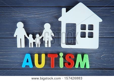 Word AUTISM with family and house on wooden background