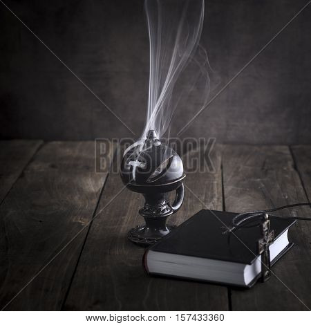 Smoking thurible burning frankincense and bible on table
