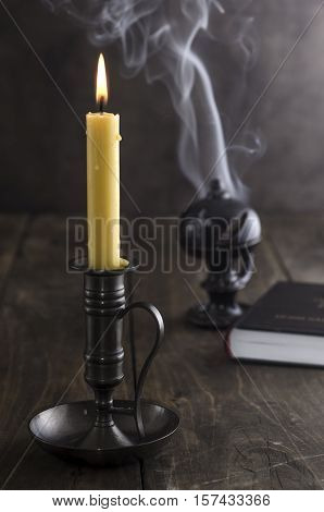 Antique candlestick and burning candle and in the background a incense holder