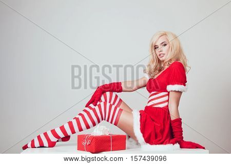 Beautiful blonde snow maiden with gift sitting on a white background