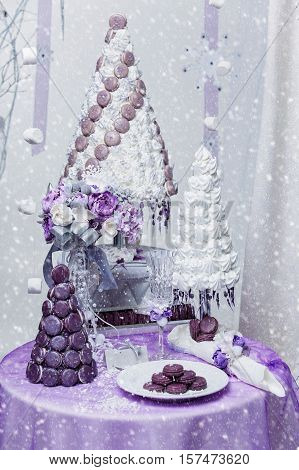 Beautiful set of three handmade white and purple croquembouche wedding cakes made from meringue and macarons standing on small dessert table