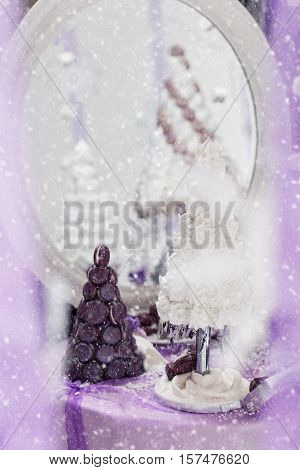 Beautiful set of three handmade white and purple croquembouche wedding cakes made from meringue and macarons standing on small dessert table reflecting in mirror