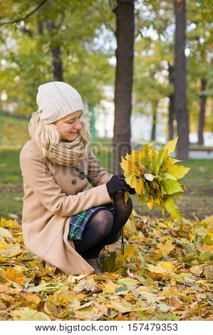 Young woman walking in the park and making bouquet of autumn nice yellow maple leaves in sunny day. Park background. Girl in the park with fall bouquet. Lifystyle and autumn concept.