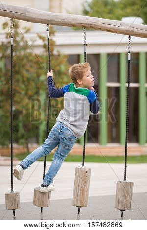 Portrait of cute kid boy playing on the climbing frame. Young boy climbing on playground during summer. Child enjoys climbing through a tunnel in a children's playground outdoors.