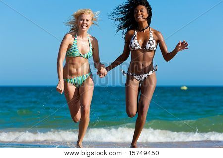 Friends -Ã?Ã? two women - on the beach having lots of fun in their vacation running through the water