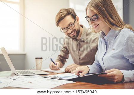 Beautiful business couple is using a laptop studying documents and smiling while working in office