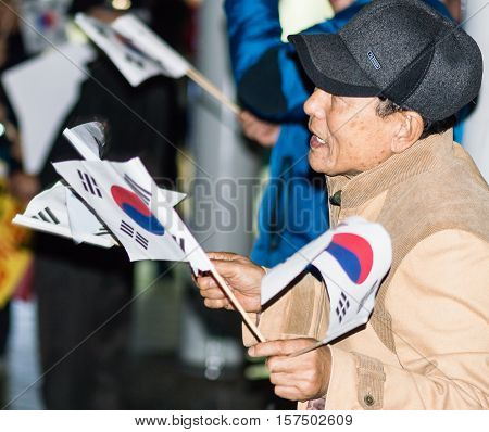 SEOUL, SOUTH KOREA, NOVEMBER 19,2016 Man waves Korean flag as part of a group of protesters outside Seoul Station rally against impeachment of President Park Geun-hye