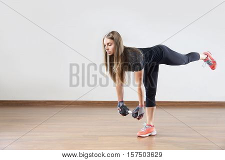 Young fit woman works out with weight in gym class. Exercise with the raised leg. Space for placing text .
