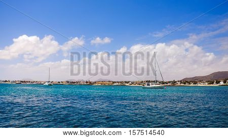 View on the ocean with blue water and white boast and the beach Corralejo with sand dunes and the town on the Canary island Fuerteventura Spain.