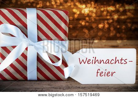 German Text Weihnachtsfeier Means Christmas Party. Macro Of Christmas Gift Or Present On Atmospheric Wooden Background. Card For Seasons Greetings, Best Wishes Or Congratulations. White Ribbon.