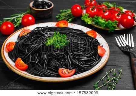 Spaghetti with ink of a cuttlefish. Ingredients for spaghetti with cuttlefish ink herbs thyme rosemary black olives lettuce. Spaghetti with cuttlefish ink decorated with cherry tomatoes.