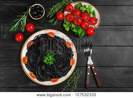 Spaghetti with ink of a cuttlefish. Ingredients for spaghetti with cuttlefish ink herbs thyme rosemary black olives lettuce. Spaghetti with cuttlefish ink decorated with cherry tomatoes. Top view.