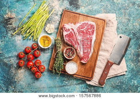 Raw T-bone Steak for grill or BBQ on cutting board over blue concrete background, top view
