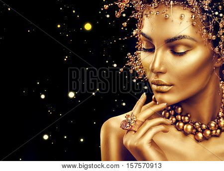 Gold Woman skin. Beauty fashion model girl with Golden make up, hair and jewellery on black background. Gold earrings, ring and necklace. Metallic, glance Fashion art portrait, Hairstyle and make up