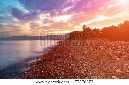 Beautiful colorful sunrise at the sea with dramatic clouds and seashore with boulders