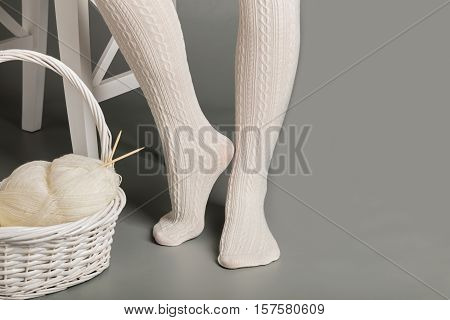 Female feet in white knitted tights near the basket with yarn and knitting.