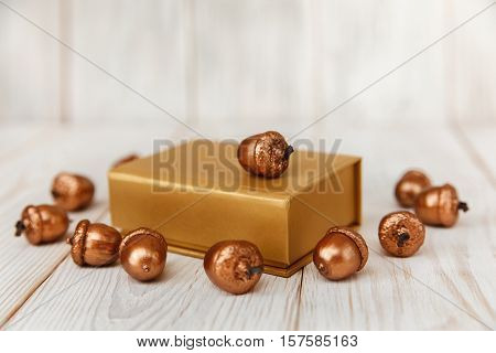 Christmas composition.Golden present box and golden acorns.White wooden table.Mokup with space.