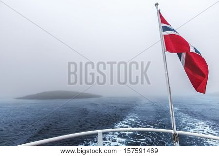Norwegian flag flying in the wind over the sea on heavy foggy day in Northern Norway