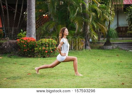 Young beautiful fitness girl with ponytail do exercises on green grass at the park.