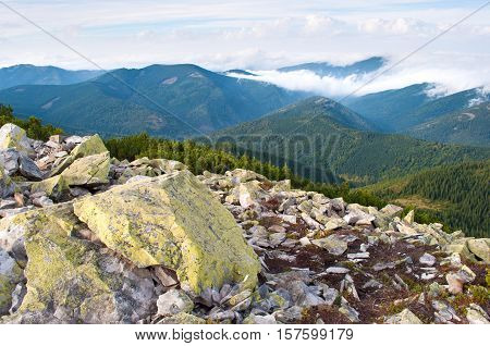 Beautiful landscape of the Carpathian mountains in autumn. Day. Large stones against the hill covered with pine forest creeping pine and fluffy white clouds