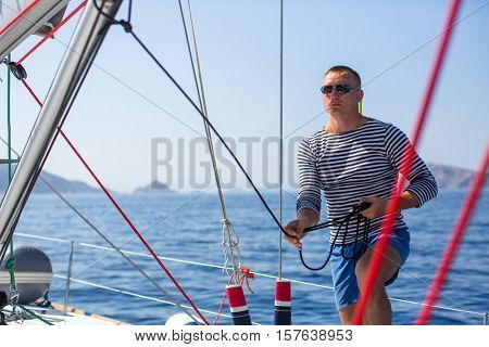 Young man skipper at his sail boat, controls ship during sea yacht race. Luxery vacations, sailing, adventure, travel.