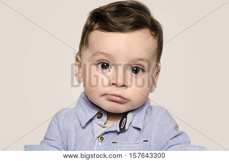 Portrait of a cute baby boy looking at camera bored. Adorable child wearing a blue shirt making cute mimic.