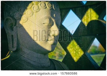 Carved stone buddha statue inside small stupa. Vintage filter with a white border