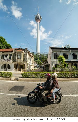 Kuala Lumpur, Malaysia - September 24, 2016: Locals drive motorbike on the street with a famous Menara KL tower at background