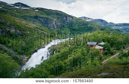 Kjosfossen waterfall valley landscape. Waterfall dam, village houses and famous Flamsbana railway. Flam, Aurland, Norway.