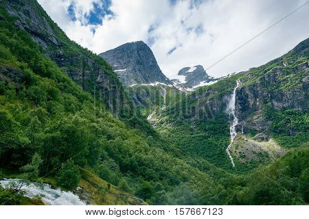 Dreamy mountain valley with green forests, rocks and waterfalls. Hiking path to Briksdalsbreen glacier. Briksdal, Norway.