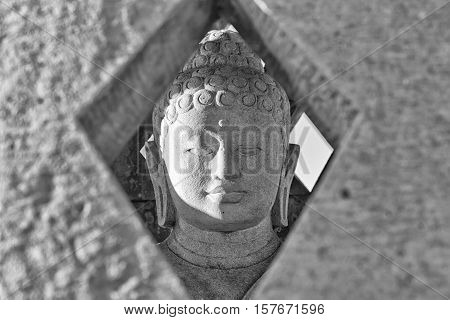 Carved stone buddha statue inside small stupa. Black and white photograph