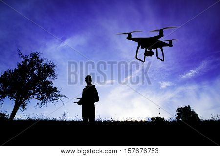 Silhouette of young man with flying drone in nature at dusk against blue sky.