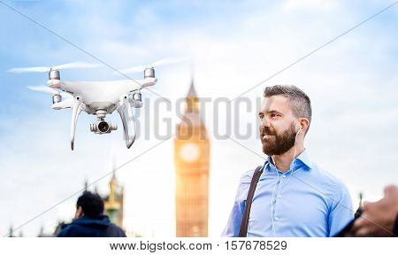 Hovering drone taking pictures of handsome young businessman in blue shirt on Westminster bridge next to Big Ben