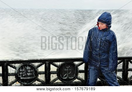 Late autumn view on the riverside with metal embankment and lonely beatyfull girl in icy splashes of storm waves.