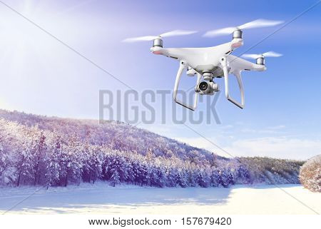 Hovering drone taking pictures of snowy white meadow and forest and clear blue sky
