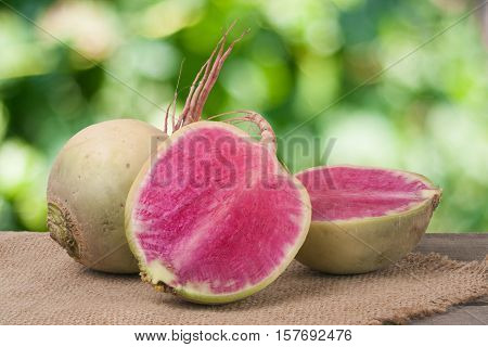 One whole and sliced watermelon radish on a wooden table with blurred garden background.