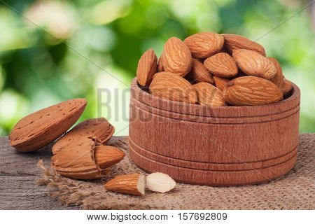 almonds in a bowl on the old wooden board with sackcloth and blurred garden background.
