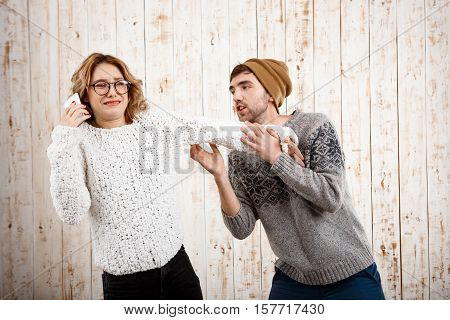 Young handsome man unnerve his girlfriend speaking on phone over wooden background. Copy space.