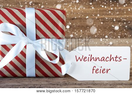 German Text Weihnachtsfeier Means Christmas Party. Christmas Gift Or Present On Wooden Background With Snowflakes. Card For Seasons Greetings. White Ribbon With Bow.