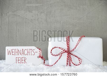 Label With German Text Weihnachtsfeier Means Christmas Party. One Christmas Gift Or Present On Snow. Cement Or Concrete Wall As Background. Modern And Urban Style.