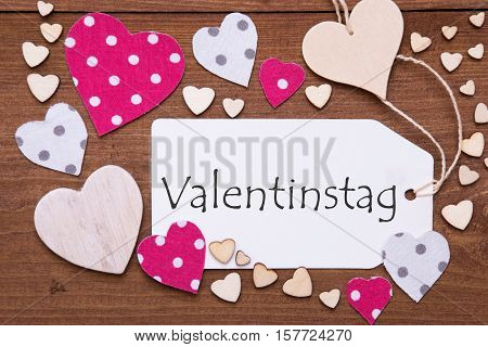 One Label With German Text Valentinstag Means Valentines Day. Flat Lay View With Wooden Vintage Background. Pink Wooden And Paper Hearts.
